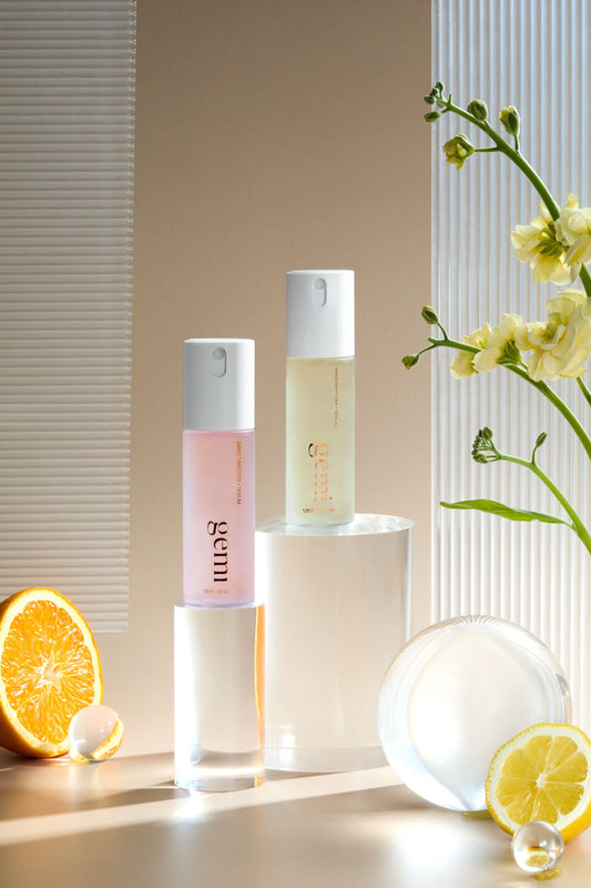 Two hand sanitizer bottles with a lemon and orange on a neutral background.