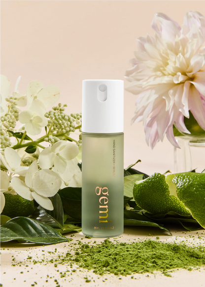 Hand sanitizer bottle labeled 'gemi' with neroli flowers and green tea leaves on a light background.